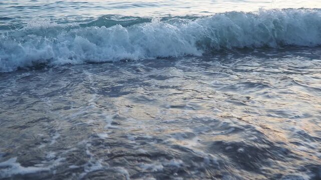 Waves gently lap at shore during stunning sunset over ocean. Golden sunlight reflects off waves as they roll onto shore, creating tranquil atmosphere at sunset by sea. Montenegro summer Canj