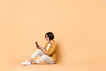 Smiling woman with smartphone sitting on beige background. Space for text