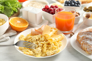 Tasty breakfast. Scrambled eggs, ham, cheese and other food served on light wooden table, closeup