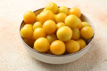 Tasty ripe plums in bowl on beige textured table, closeup
