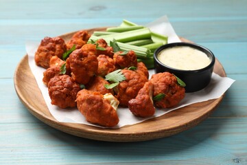 Baked cauliflower buffalo wings with celery and sauce on light blue wooden table, closeup