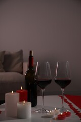 Burning candles, wine and paper hearts on table indoors