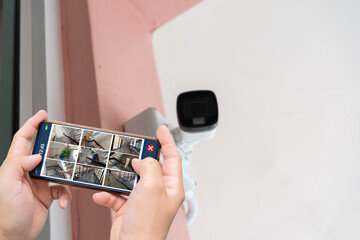 Person hand holding smartphone with multiple camera views of office locations. Surveillance, modern...