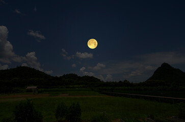 Bright full moon over the field and mountains in the evening