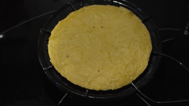 Flipping the Arepa on the Grill for Even Cooking. Cook&rsquo;s hands skillfully flip an arepa on the grill, ensuring both sides are evenly cooked