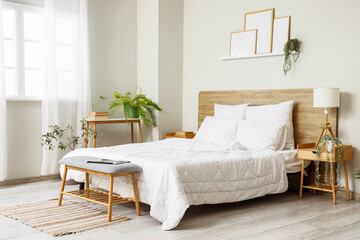 Interior of light bedroom with cozy bed, houseplants and wooden bedside table