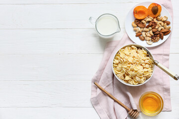 Napkin, nuts and bowl with cornflakes on white wooden background