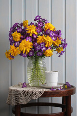 retro composition, violet phlox and yellow rudbeckia in a glass vase on the table with a lace knitted napkin. garden flowers.