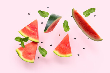 Flying pieces of fresh watermelon with mint and seeds on pink background