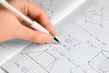 Female hand writing maths formulas in copybook, closeup