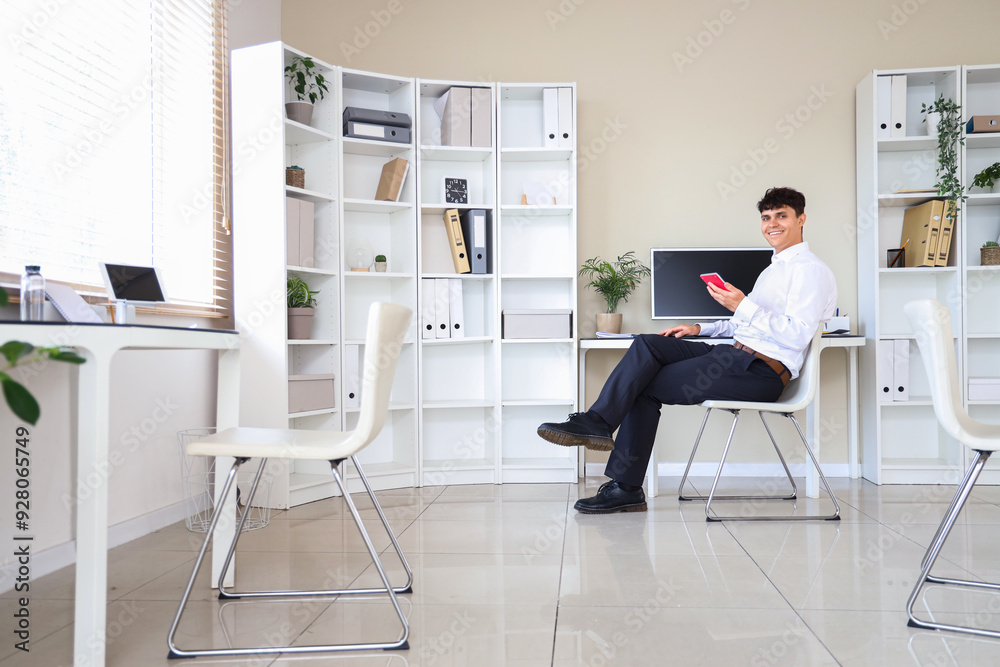 Poster male accountant holding calculator and sitting at workplace with modern computer in office