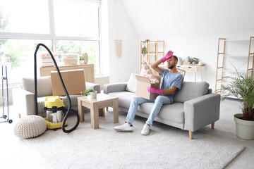 Tired male janitor holding cardboard box and sitting on sofa in room