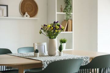 Wild flowers in vase on dining table and chairs in room