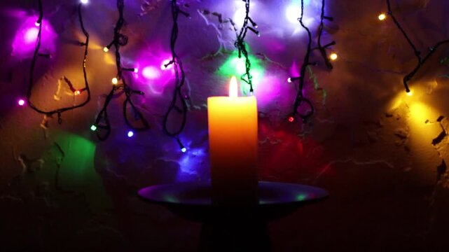 Primer plano de una vela blanca con llama rodeada de varias luces con bombillos de varios colores en movimiento en la oscuridad - Powered by Adobe