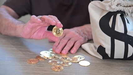 old retiree holds a token bitcoin souvenir in his hand seated by a bag of cash