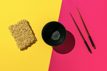 Instant Noodles with Black Bowl and Chopsticks on Vibrant Yellow and Pink Background