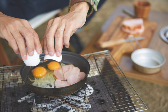 屋外でフライパンに卵を落とす男性の手元