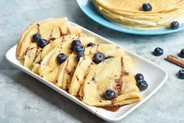 A serving of pancakes on a plate with blueberries and drizzled with chocolate glaze