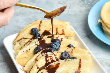 A serving of pancakes on a plate with blueberries and drizzled with chocolate glaze
