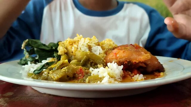 A boy from Indonesia eats balado chicken with gusto. Balado chicken is one of the menus of Padang rice besides rendang. Eating using bare hands without spoons. A unique eating habit in Indonesia