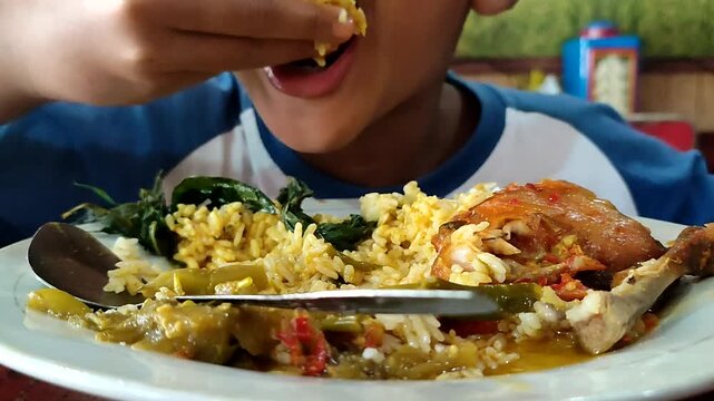 A boy from Indonesia eats balado chicken with gusto. Balado chicken is one of the menus of Padang rice besides rendang. Eating using bare hands without spoons. A unique eating habit in Indonesia
