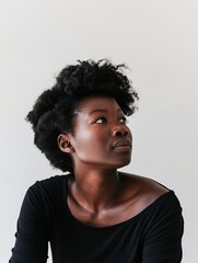 Obraz premium Close-up portrait African American woman with natural curly hair, wearing black shirt, image is taken in minimalist studio setting with pure white backdrop, capturing thoughtful expression.