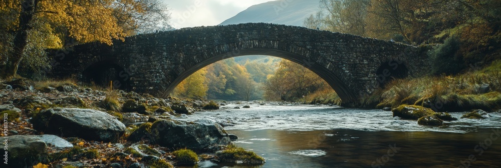 Canvas Prints A rustic stone bridge arches over a flowing river, surrounded by vibrant autumn foliage. The image evokes a sense of tranquility, nature, and the beauty of the changing seasons.