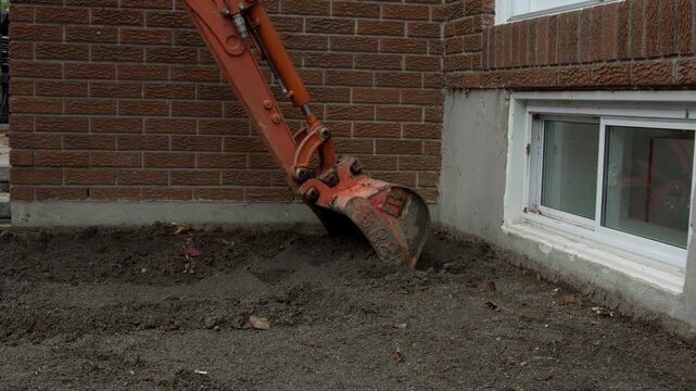Mini excavtor picking up bucket of soil from beside residential house - digging out foundation - side profile