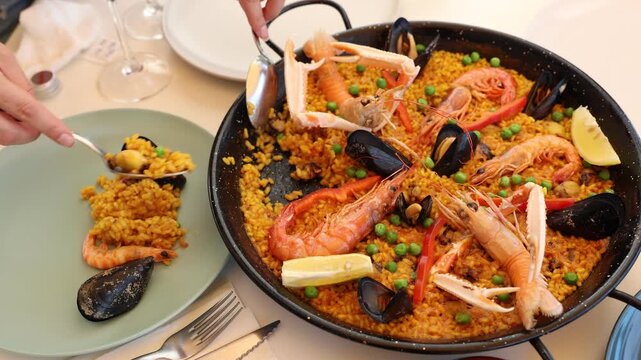 Womens hands lay out sea paella in plates for family dinner. Women hands are divided into portions of paella cooked in pan with lobsters, shrimp, mussels. 