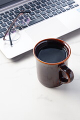 コーヒーを飲みながらノートパソコンでデスクワークをしているイメージ

