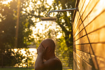 Man under sunset outdoor shower. Concept of relaxation and refreshing water experience