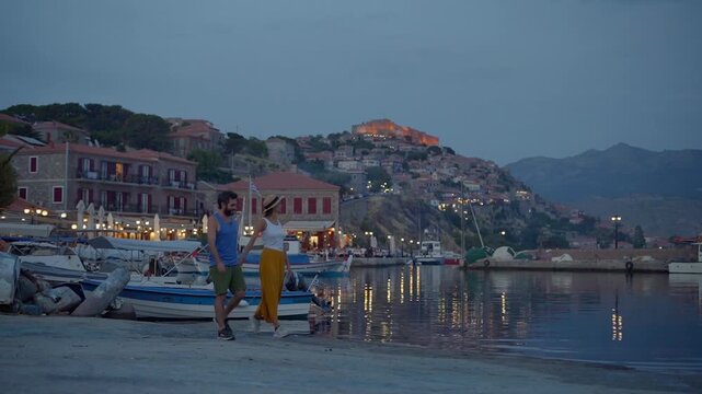 A lovely European couple walking hand in hand while exploring beautiful town of Molyvos in the evening with Castle of Mithymna in background