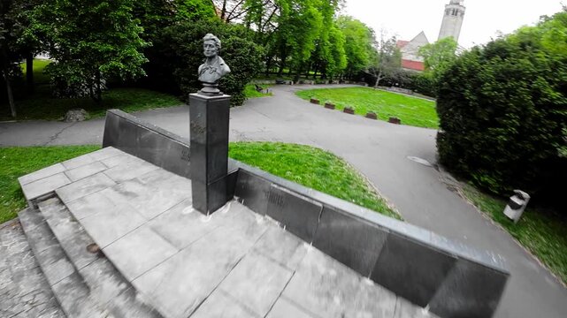 The video begins with a view of a park in Opole, Poland. The park is filled with lush greenery, including trees, bushes, and flowers. There is a monument to the poet Adam Mickiewicz in the center of