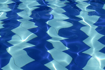 A close-up of light reflecting on the rippling water surface in a swimming pool lined with bright and dark blue tiles