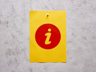Information info sign on a yellow sheet of paper pinned to a white concrete wall.