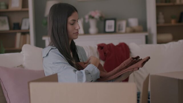 A beautiful woman at home chooses clothes for a donation sorting wardrobe. Donations and moving house concept. 4K
