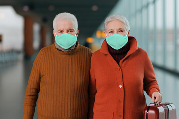 Senior couple wearing mint green masks in a modern airport terminal, embracing travel with a small suitcase and expressing resilience during health precautions.