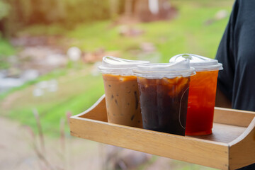 A waiter serving cold drinks, iced coffee and iced tea on a wooden tray in a cafe
