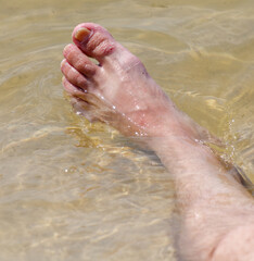 Close-up of a man's foot in the water of the sea along the sandy shore