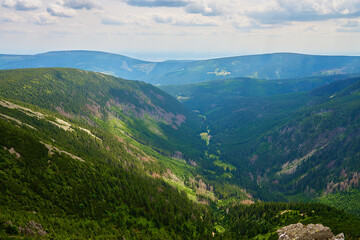 Beautiful panoramic view of green mountain valley with rolling hills and dense forests under cloudy sky. Travel tourism and hiking concept