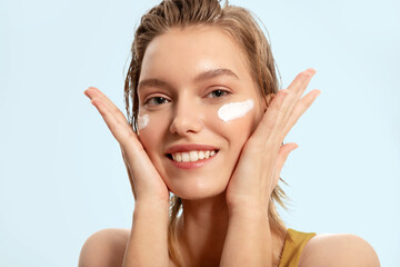 Smiling woman put cream on her face, protection. Cream protects skin from photoaging and harmful effects ultraviolet rays.