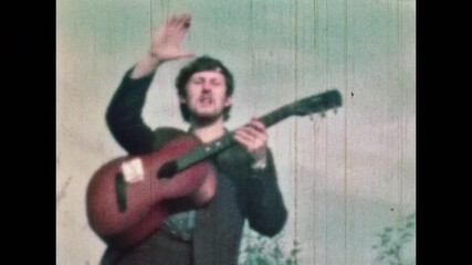 Film archive, Handsome musician playing guitar, smoking cigarette on blue sky outdoors. Smiling passionate man strumming on music instrument. Happy, joy artist portrait. Vintage color Retro 1960s