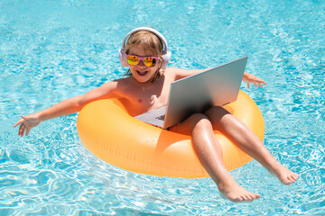 Child with laptop in swimming pool in summer day. Summer business and online technology.