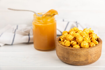 Sweet caramel popcorn in a bowl on a wooden background. Salted caramel popcorn. Caramel sauce. Close up. Topping. Place for text. Copy space