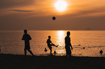Fototapeta premium Silhouettes of Asian men playing beach soccer on a beach by the sea at sunset