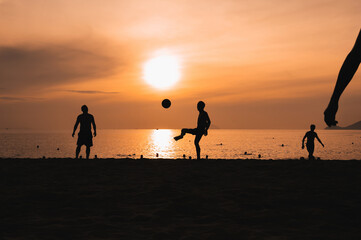 Silhouettes of Asian men playing beach football on beach by the sea at sunset