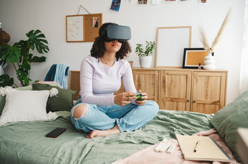 Girl wearing virtual reality simulators holding game controller on bed at home