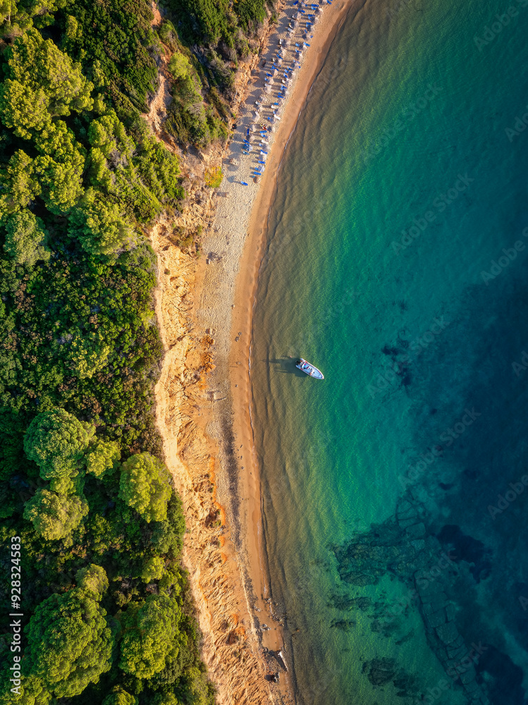 Wall mural aerial overhead sunset view of mantraki beach with emerald sea and lush pine tree forrest at the isl