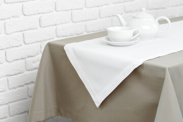 Beige Tablecloth on White Brick Wall With Teacups and Teapot