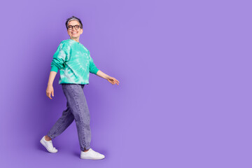 Full length photo of lovely pensioner lady walking empty space dressed stylish green garment isolated on purple color background